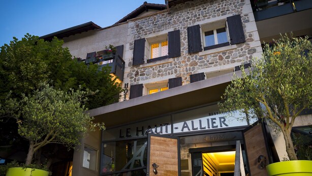 Un hotel con fachada de piedra, contraventanas de madera y un letrero que dice "LE HAUT-ALLIER".