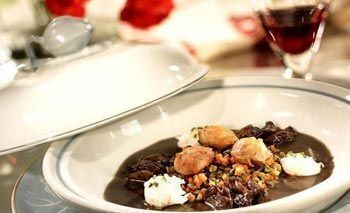 Un bol contenant de la nourriture, avec un bord blanc et un centre foncé, probablement un ragoût ou une soupe, agrémenté de morceaux de viande et de légumes.