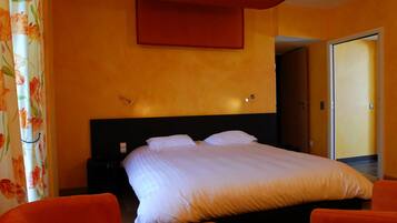A hotel room with a bed, two orange chairs, a nightstand, and a door leading to another room.