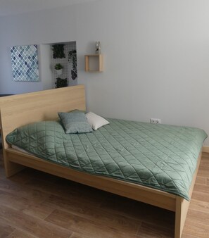 A single bed with a green quilt, a wooden headboard, and a small bedside table with a decorative item. - Hotel Restaurant Du Haut-Allier (Alleyras)