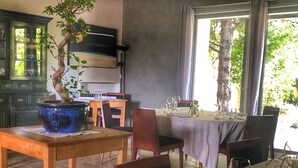 Un coin repas avec une table dressée pour deux personnes, une plante en pot et une vue sur les arbres par la fenêtre.