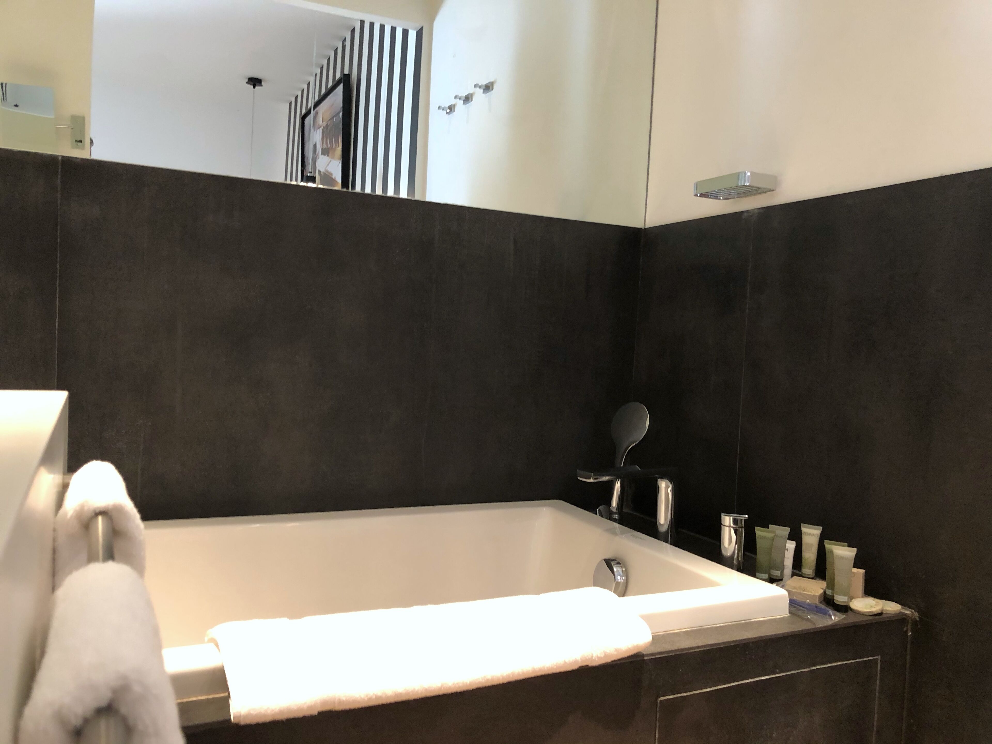 Ein modernes Badezimmer mit einer großen Badewanne, einem Handtuchhalter und Toilettenartikeln am Waschbecken.