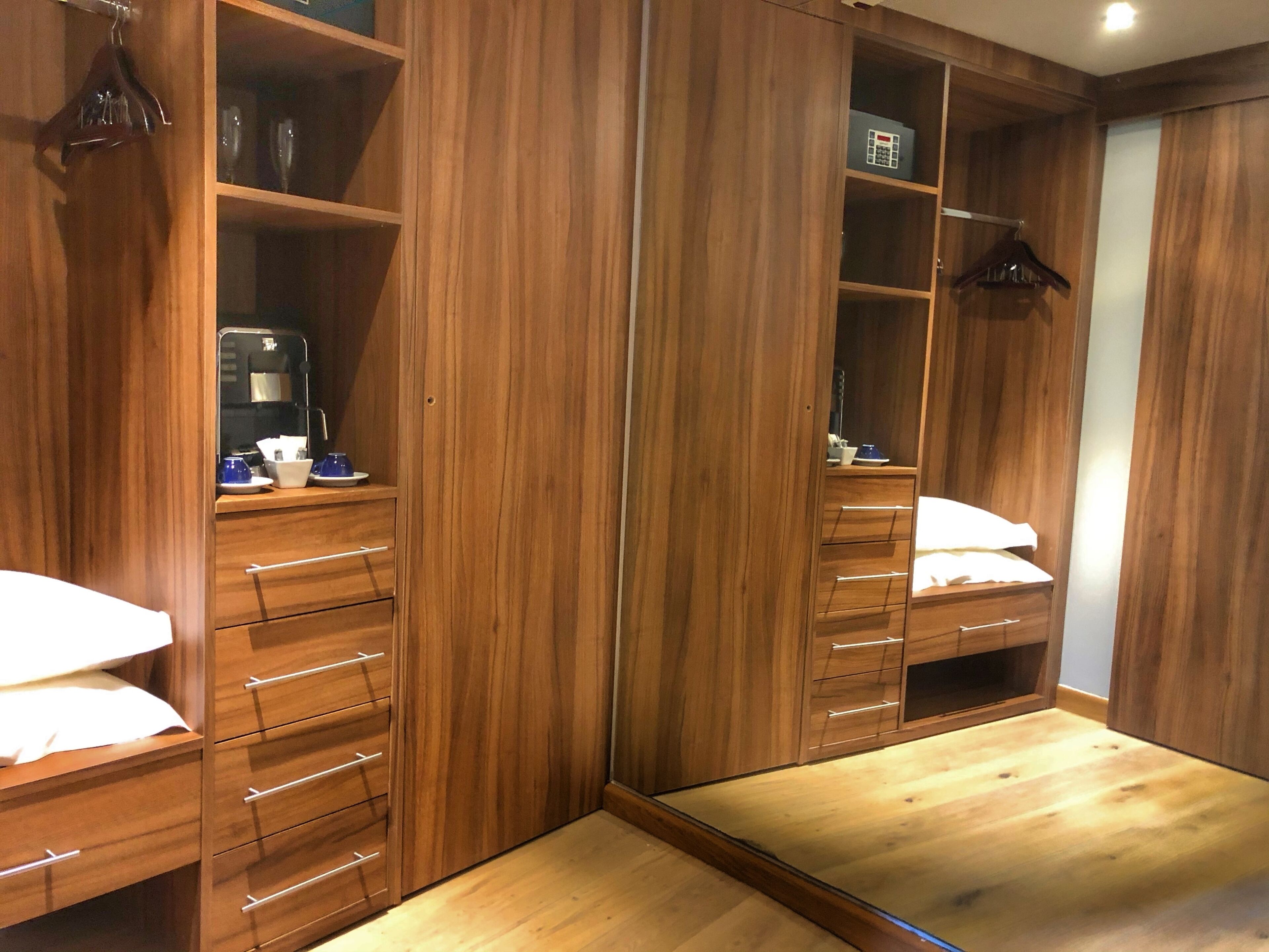 A walk-in closet with multiple wooden drawers and shelves, a mirror, and a small table with a lamp.