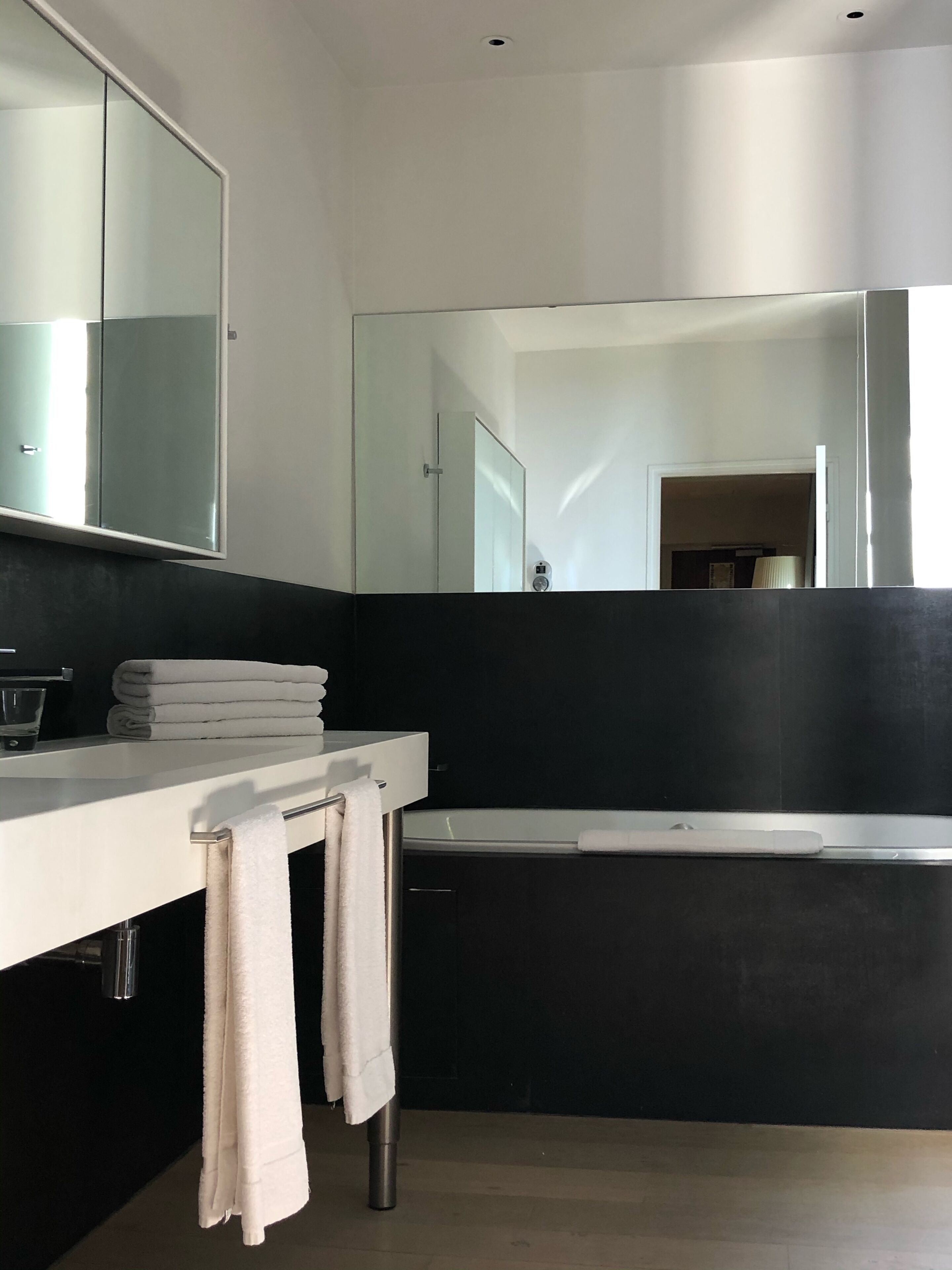 Un baño moderno con un espejo grande, una encimera blanca y una bañera negra.