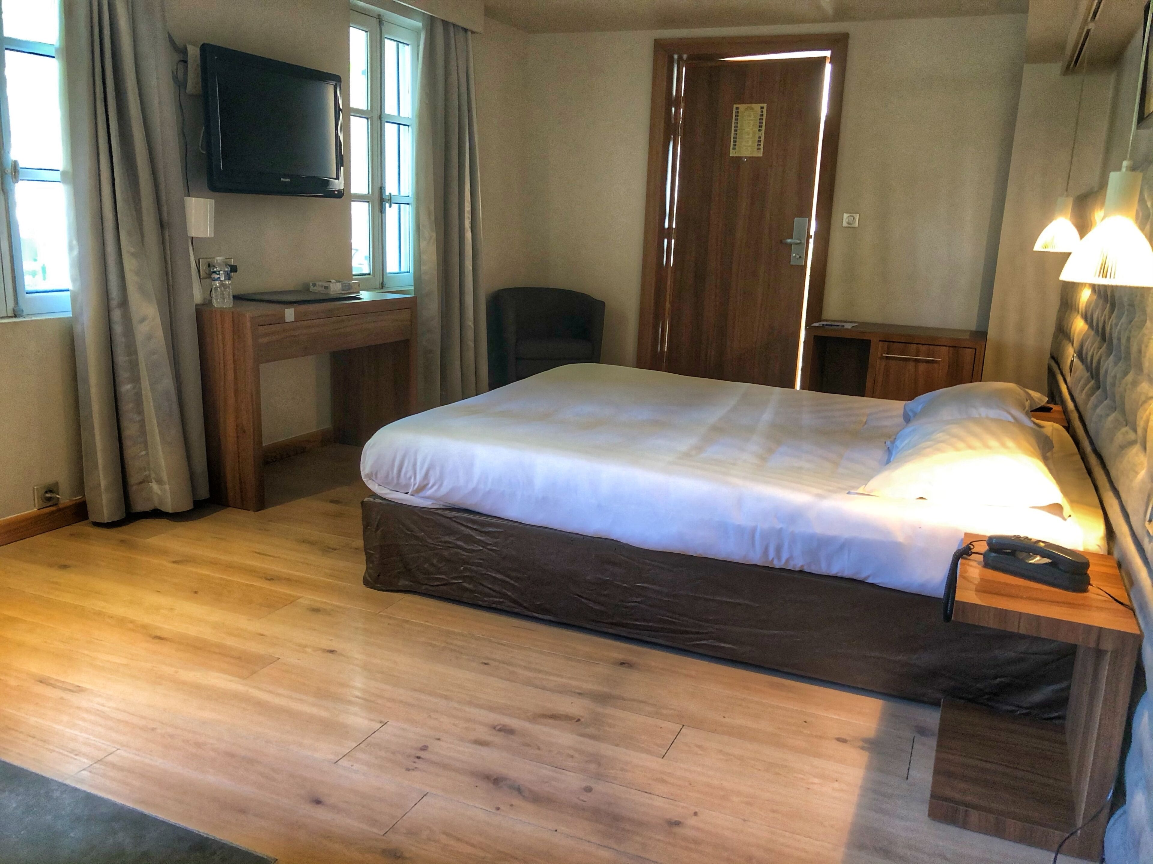 Habitación de hotel con cama, escritorio con computadora, silla, televisor y puerta.
