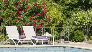 Un espace aménagé au bord de la piscine, comprenant deux chaises longues, une petite table avec un chapeau et une rambarde.