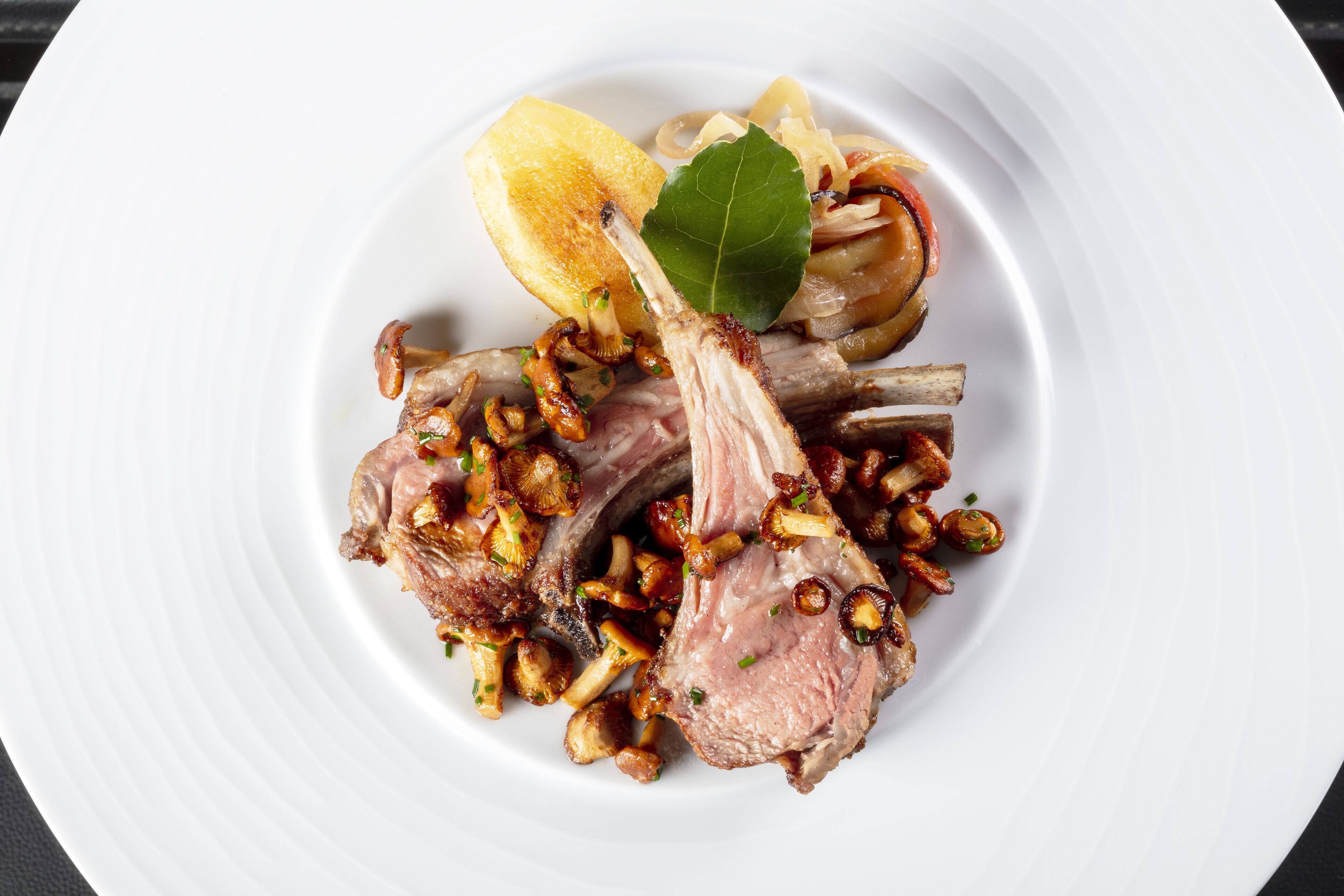 A plate of food with lamb chops, mushrooms, and a lemon wedge.