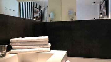 Ein modernes Badezimmer mit einem weißen Waschbecken, einem Stapel weißer Handtücher und einem großen Spiegel, der den Raum widerspiegelt.