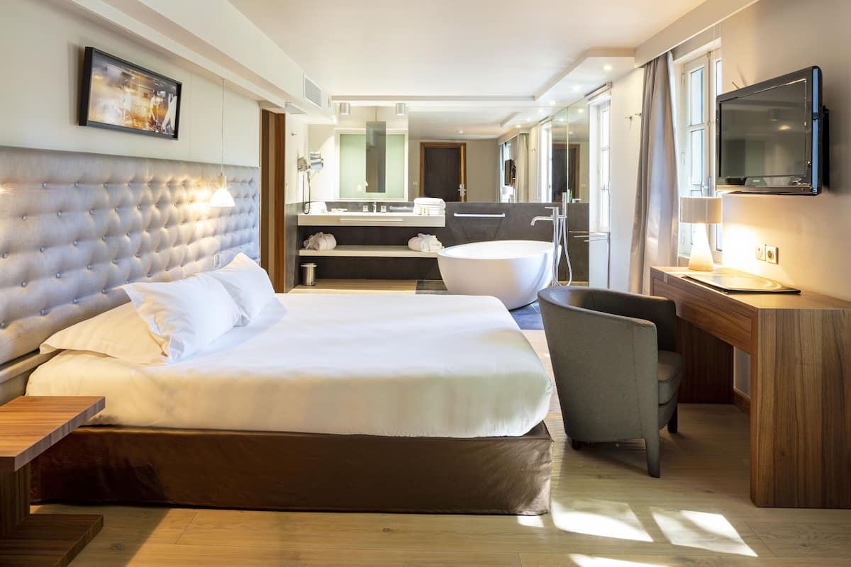 Una habitación de hotel moderna con una cama grande, una zona de estar con una silla, un escritorio, una bañera y un televisor.