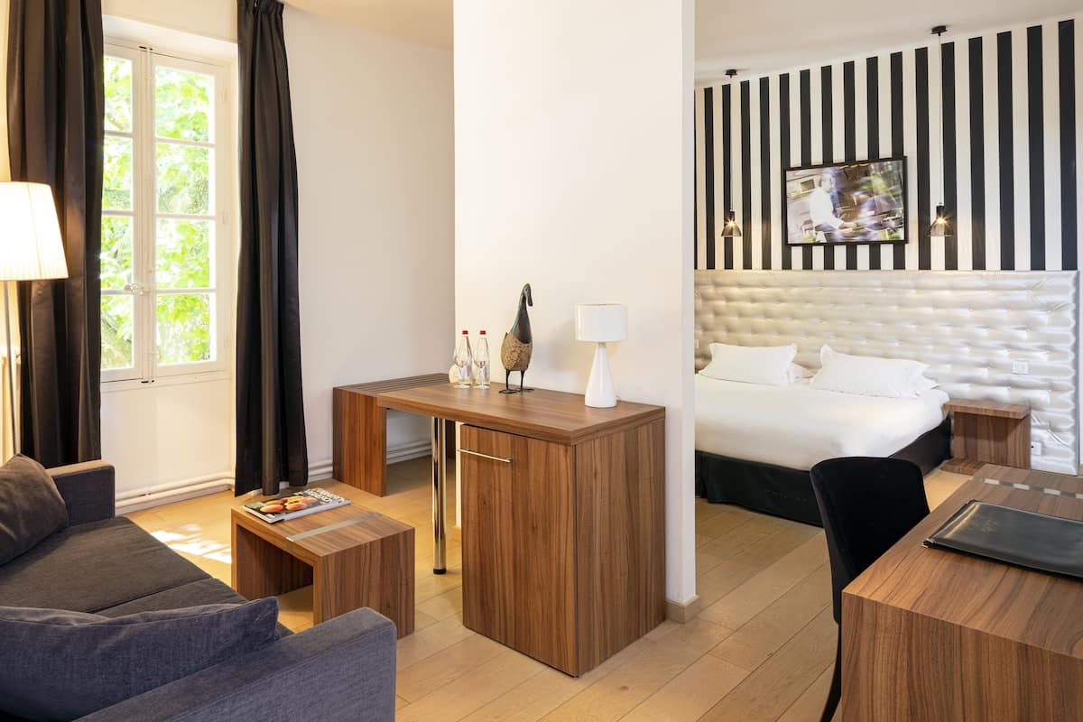 Una habitación de hotel moderna con sofá, un escritorio de madera, una cama con cabecera capitonada y un televisor montado en la pared.