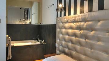 Una habitación de hotel moderna con cabecera capitonada, un espejo grande, una tocador con lavabo y una lámpara colgante.