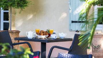 Un espacio de comedor al aire libre con sillas de mimbre, una mesa dispuesta con alimentos para el desayuno y un farol fijado a la pared.