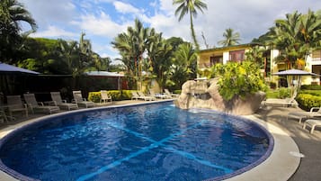 Una piscina con sillones de descanso y palmeras.