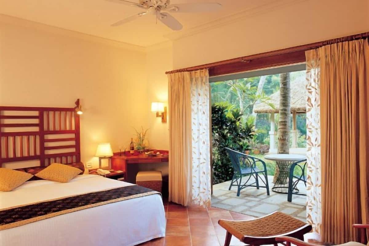 A hotel room with a bed, a desk with a lamp, a chair, and a view of the outdoors.