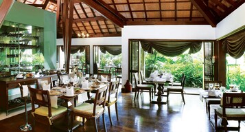 Un restaurante con mobiliario de madera, ventanas amplias y vistas a zonas verdes.