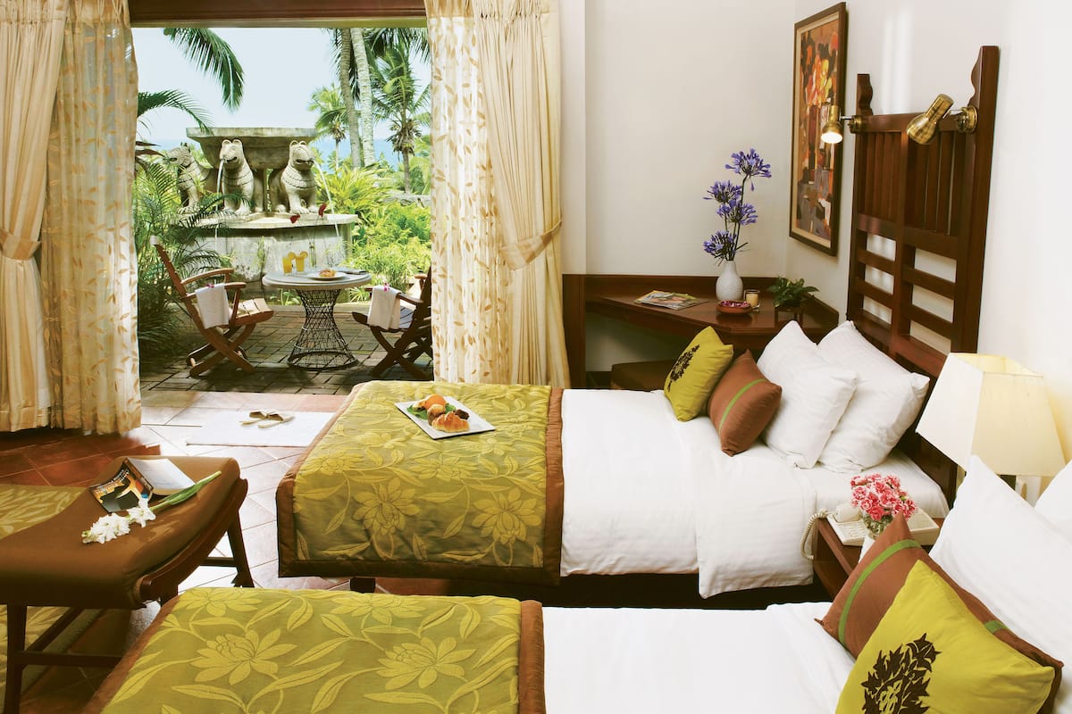 A hotel room with two beds, a dining area with a table and chairs, and a view of palm trees and a pool.