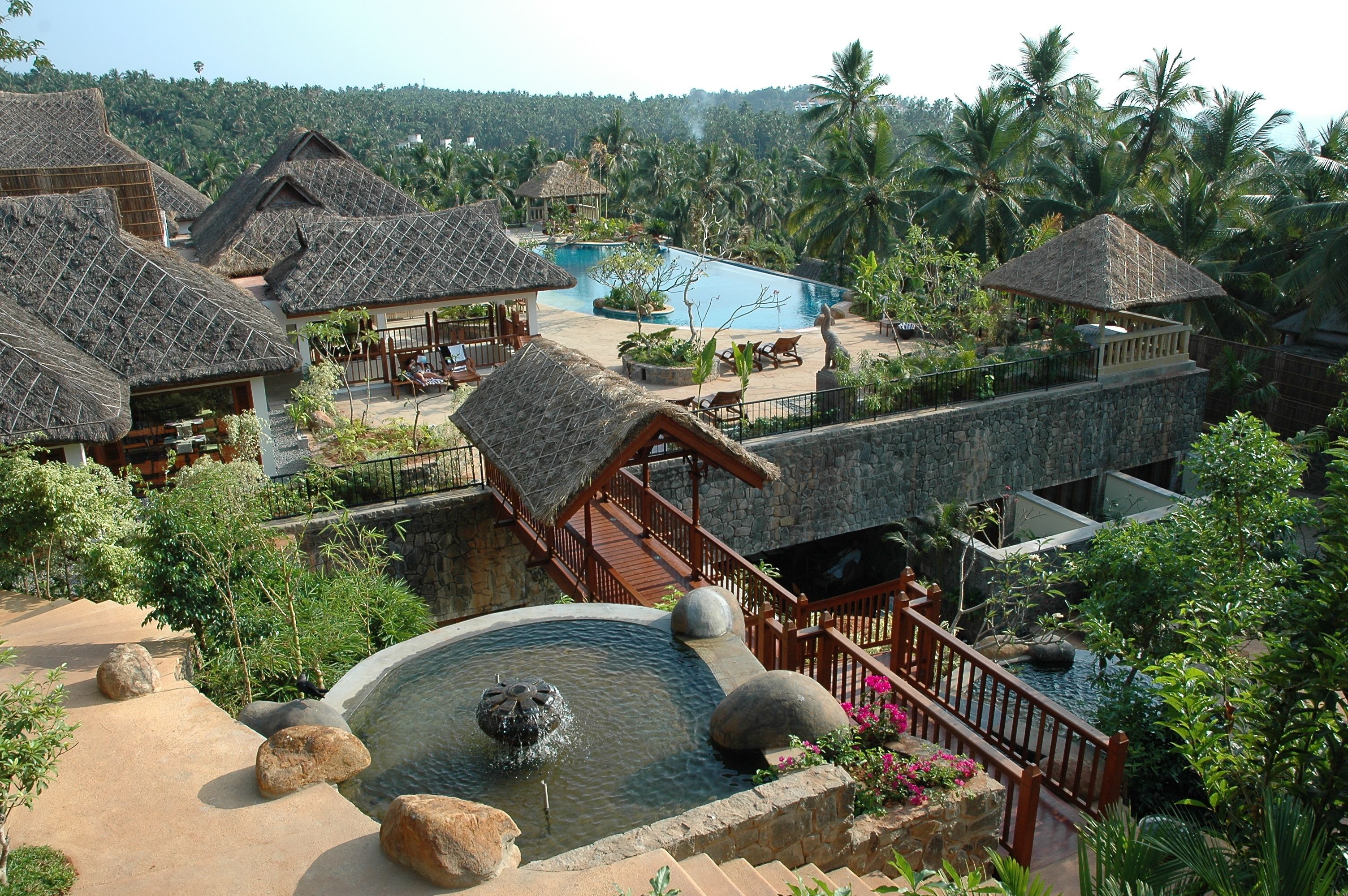 A resort with thatched-roof buildings, a swimming pool, and a water feature.