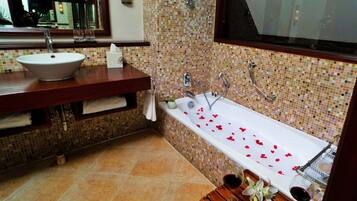 A bathroom with a white sink, a bathtub with rose petals, and a wooden vanity.