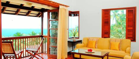 A room with a wooden floor, yellow sofa, and a table with a vase and fruit.