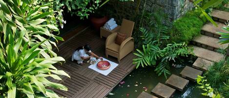 A wooden deck with a chair and a table, a stone wall, and a small pond with stepping stones.
