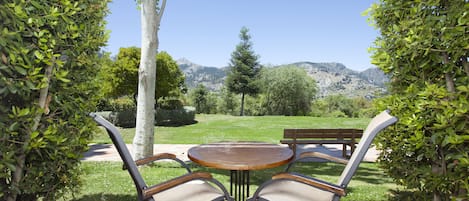 Een terras met een ronde tafel en vier stoelen, omringd door groen en uitzicht op een berg.