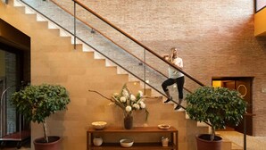 A staircase with a woman ascending, flanked by two potted plants and a wooden bench with bowls and a vase.