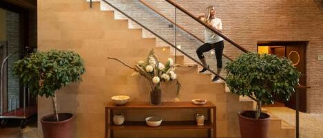 A staircase with a woman ascending, flanked by two potted plants and a wooden bench with bowls and a vase.