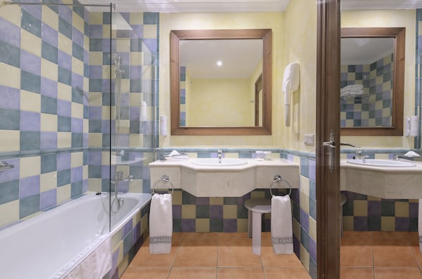 A bathroom with a checkered tile wall, two sinks, a bathtub, and a mirror. - Hotel Fuerte Grazalema (Grazalema)