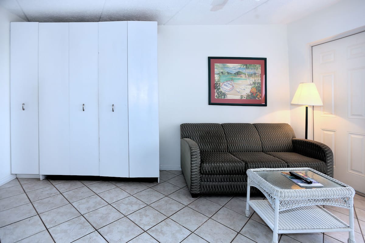 A room with a white wardrobe, a wicker sofa, a glass coffee table, and a framed picture on the wall.