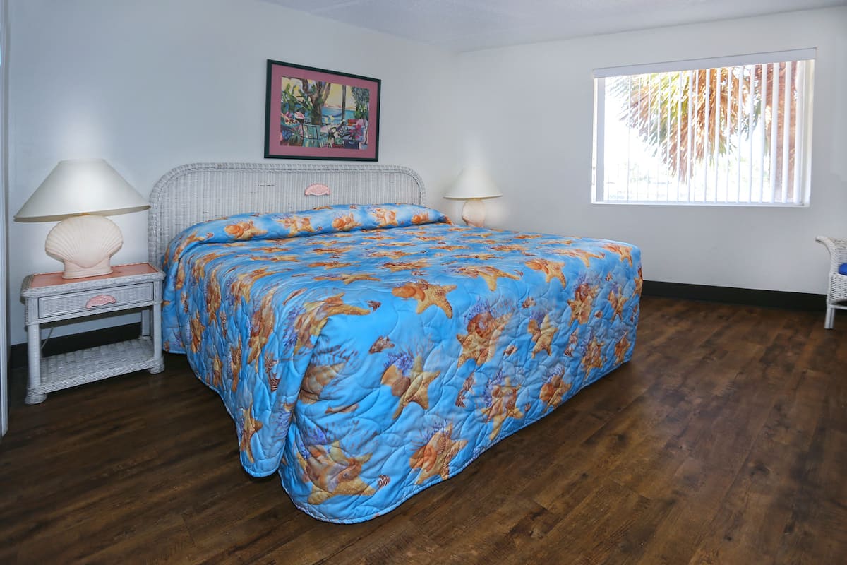 A bedroom with a bed, two bedside tables, a window, and a painting on the wall.
