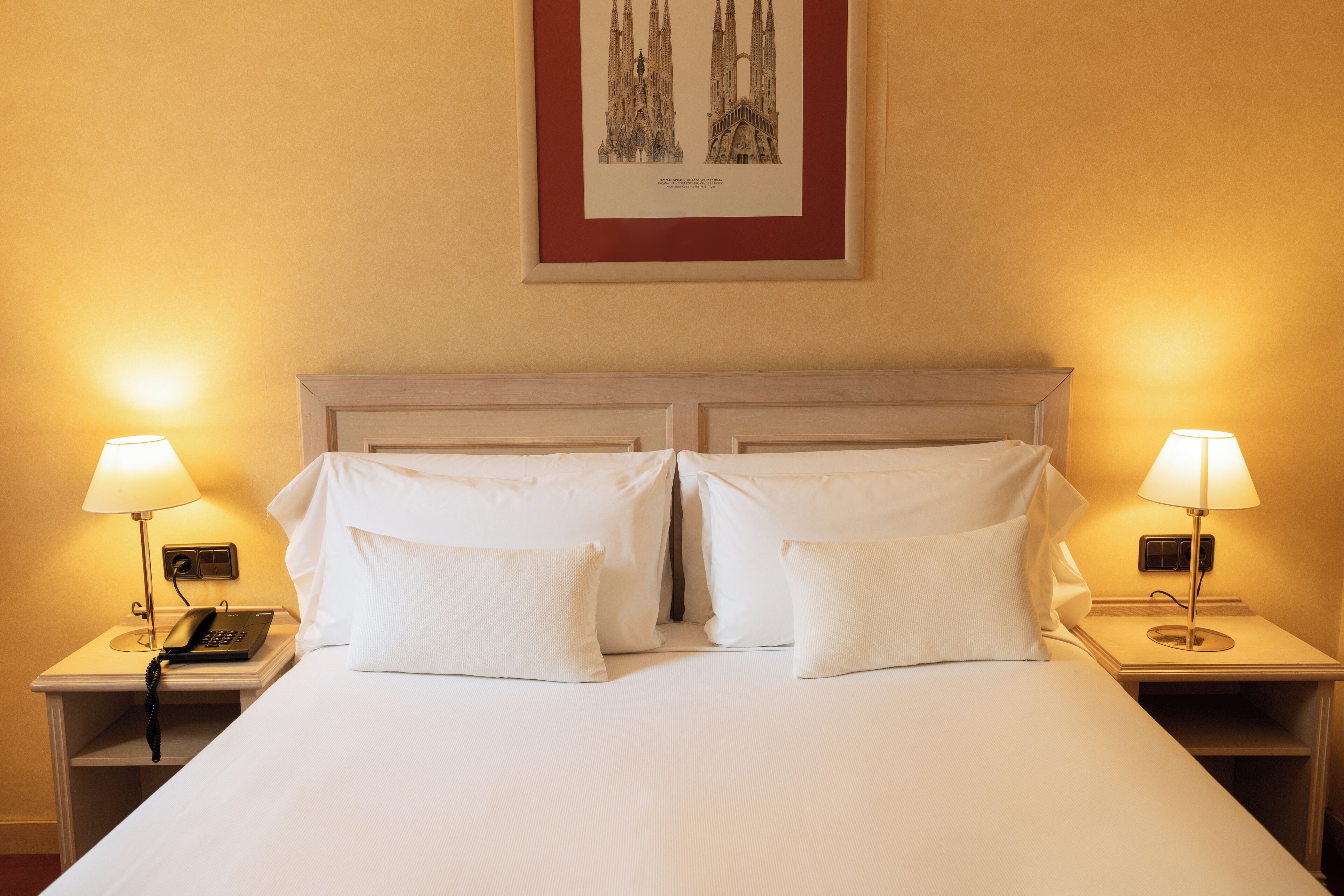 Una habitación de hotel con una cama grande, dos mesitas de noche, un teléfono y dos lámparas.
