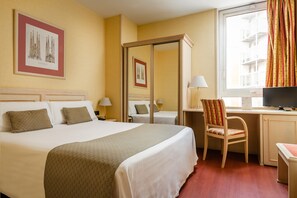 A hotel room with a large bed, a desk with a chair, a television, and a window with curtains. - Sunotel Aston (Barcelona)