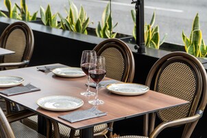 A dining table set with plates, cutlery, and wine glasses, surrounded by wicker chairs.