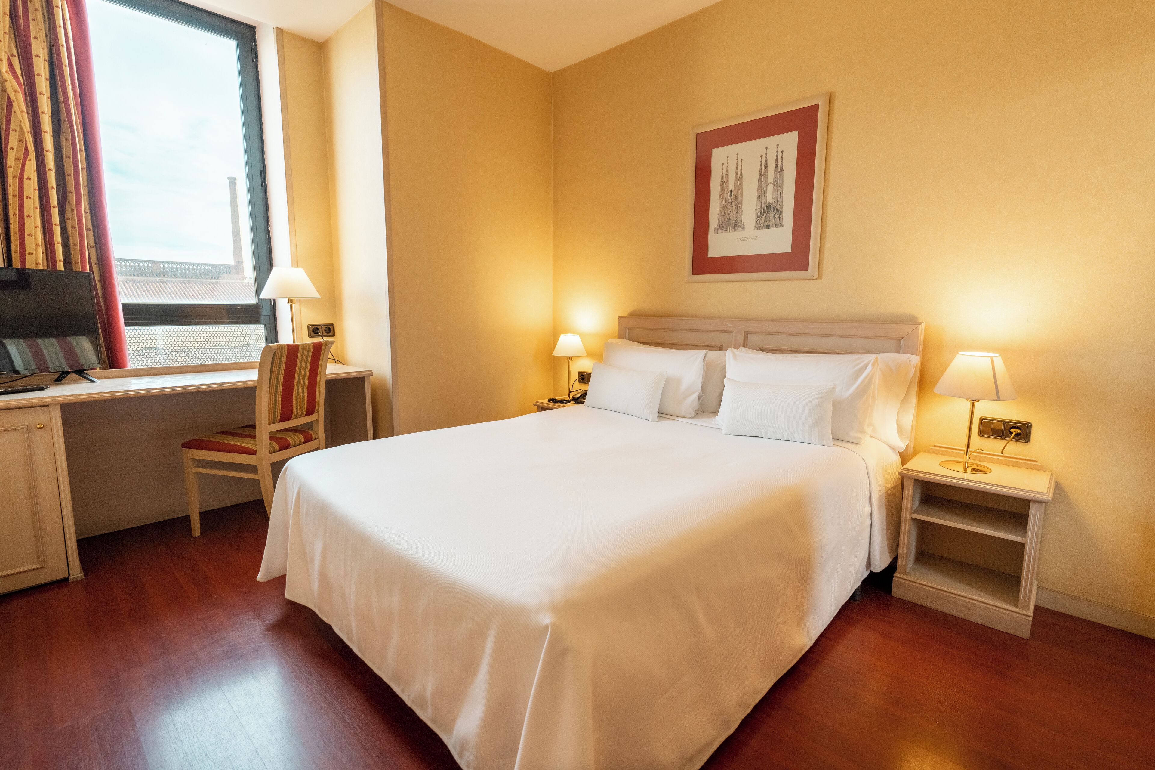 Een hotelkamer met een groot bed, twee nachtkastjes met lampen, een stoel, een bureau met een televisie en een raam met gordijnen.