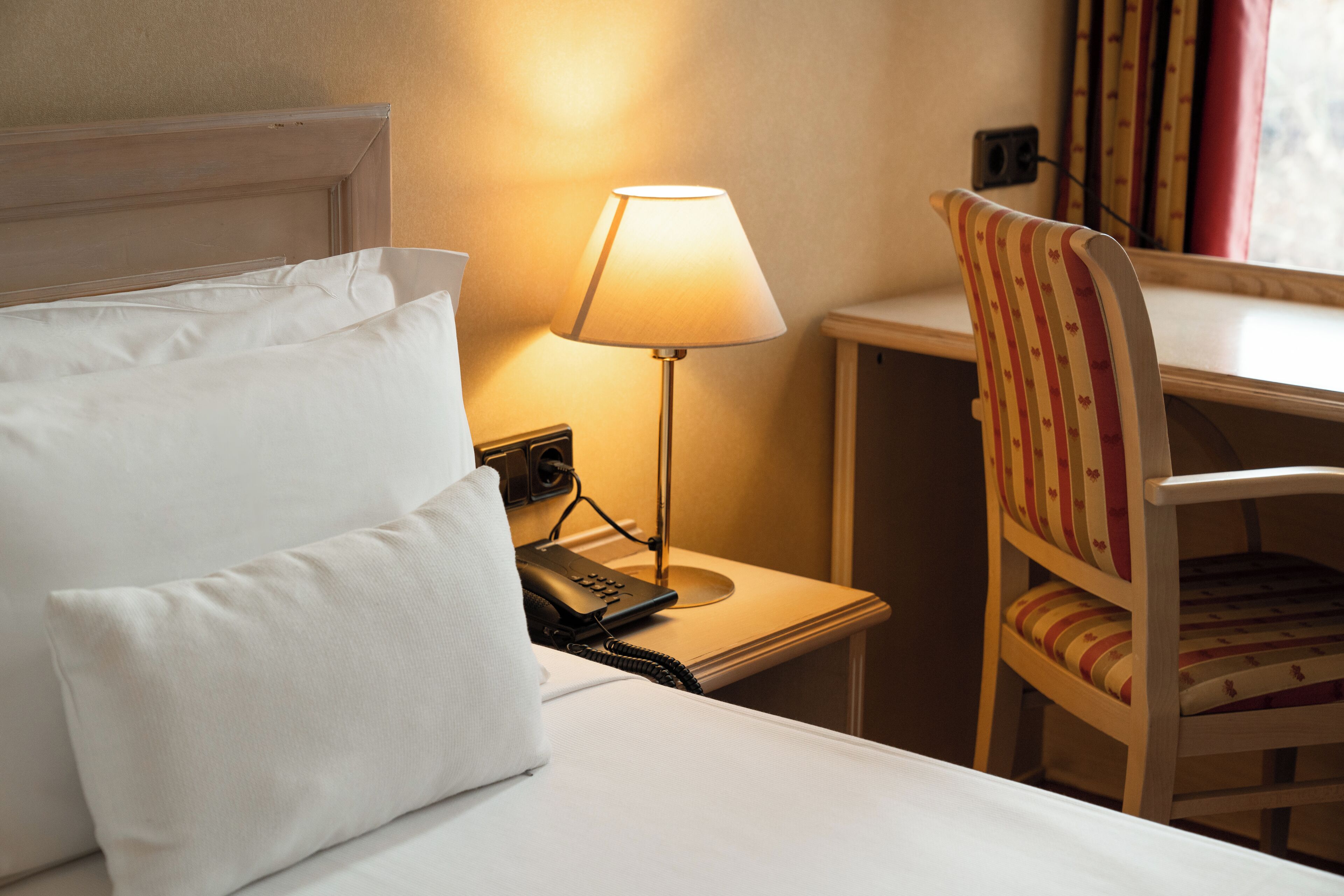 Habitación de hotel con una cama, una lámpara de noche, un teléfono y una silla a rayas.