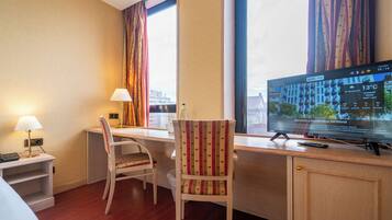 Een hotelkamer met een bureau, twee stoelen, een televisie en een raam met gordijnen.