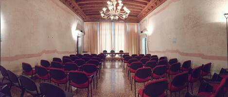 A conference room with rows of red chairs, a wooden ceiling, and a chandelier.