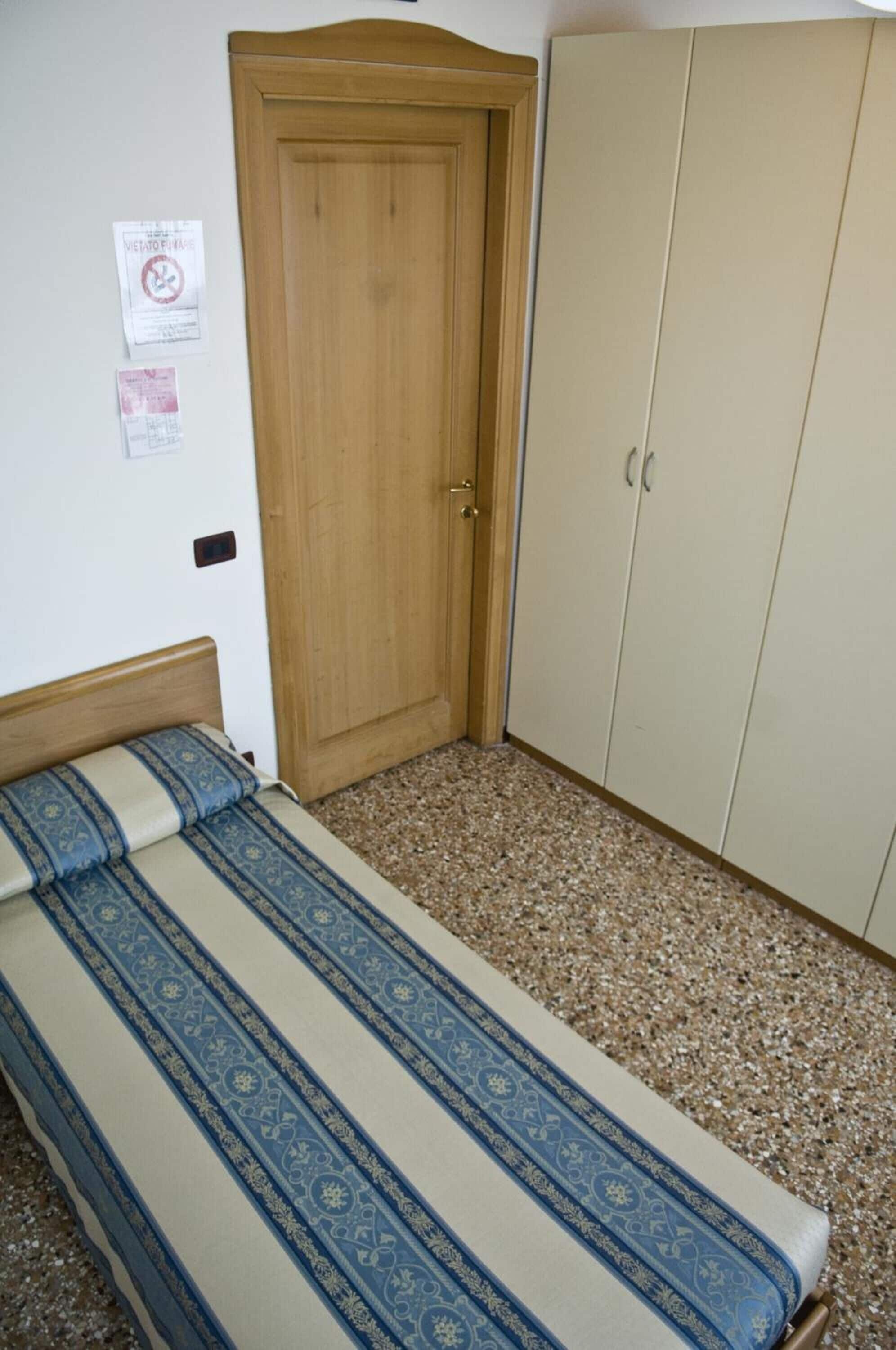 A bedroom with a wooden door, a bed with patterned bedding, and a wardrobe.