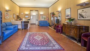 Un hall con mostrador de recepción, sofás azules, alfombra estampada y un mueble de madera con una planta.