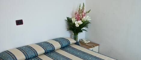 A neatly made bed with a patterned bedspread, a bedside table with a telephone, and a small potted plant on the nightstand.