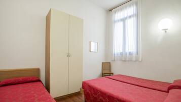 Ein Zimmer mit zwei Einzelbetten, einem Kleiderschrank, einem Sessel und einem fenster mit Vorhängen.