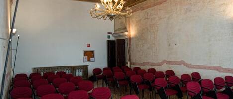 A room with rows of red chairs, a chandelier, and a wooden ceiling.