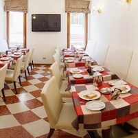 Ruokailutila, jossa on ruutukuviollinen lattia, valkoiset tuolit ja pöydät, joilla on lautaset ja aterimet.
