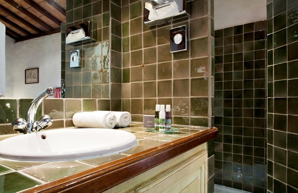 A bathroom with a white sink, green-tiled walls, and a wooden countertop.
