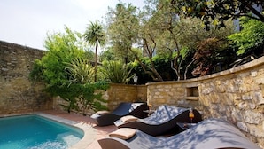 Un espace aménagé au bord de la piscine, avec des chaises longues et un mur en pierre.