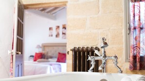 Une salle de bain avec un mur en pierre, un robinet de style rétro et une fenêtre agrémentée d’un rideau coloré.