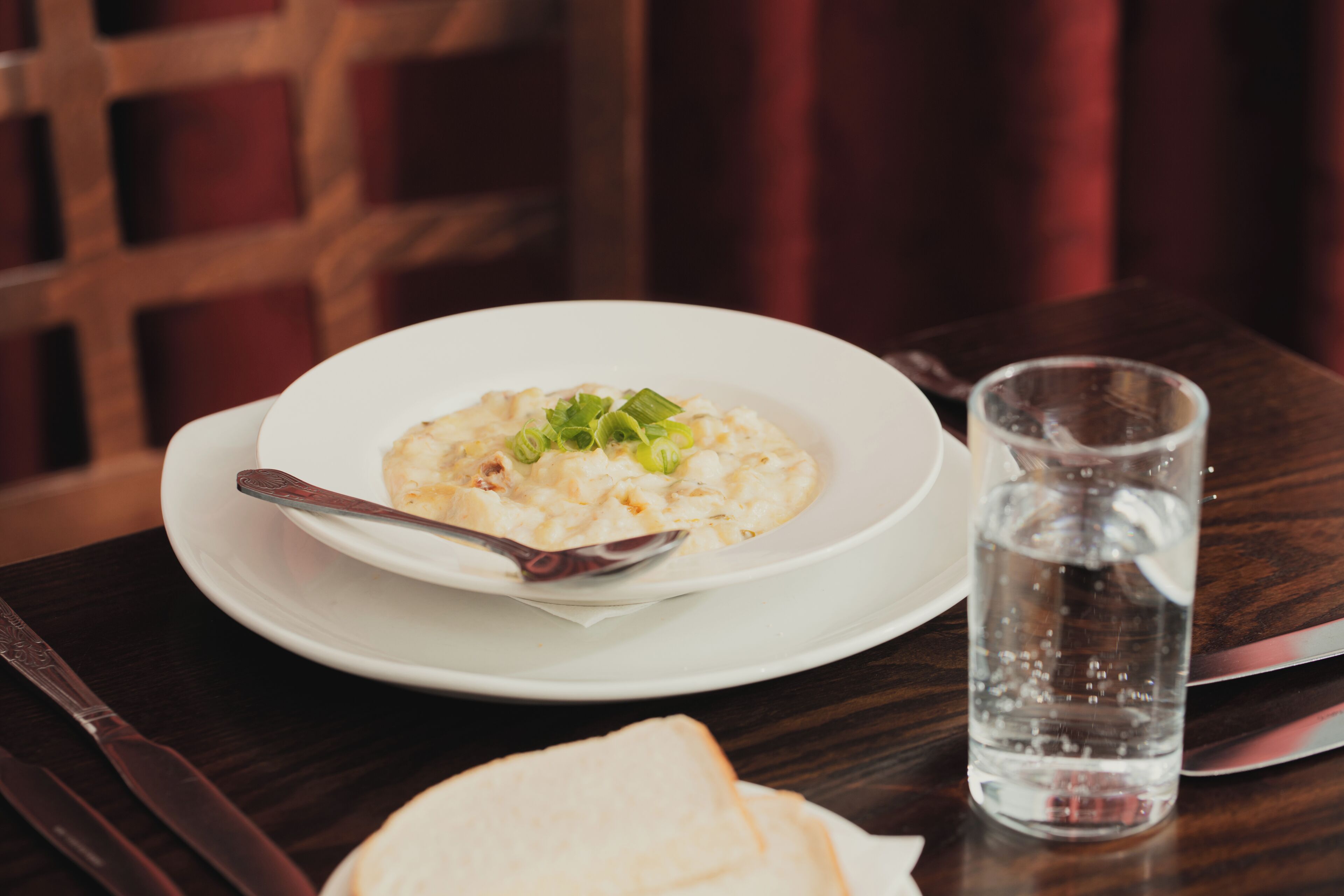 A dining table with a bowl of soup, a glass of water, and a plate of bread.