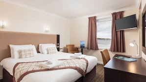A hotel room with a large bed, a desk, a chair, a TV, and a window with curtains. - Dunollie Hotel (Strath)