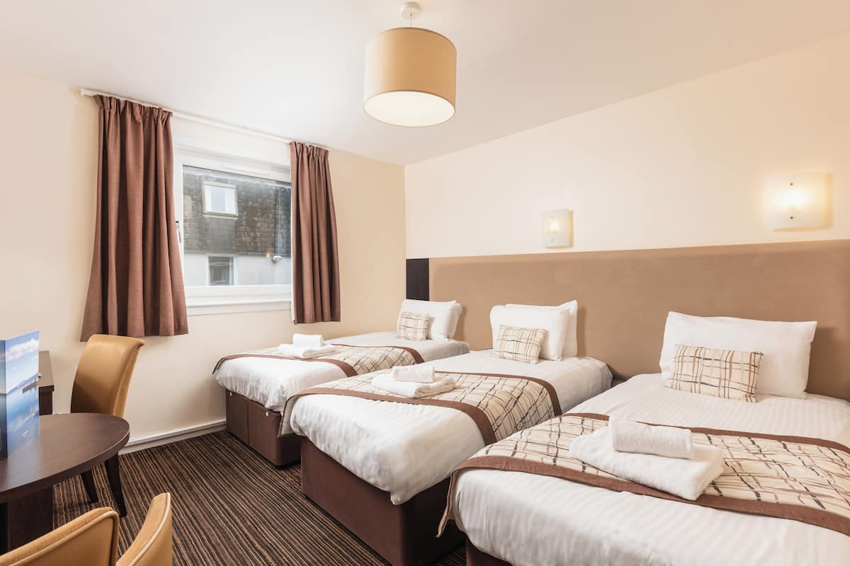 A hotel room with three beds, a desk, and a chair.