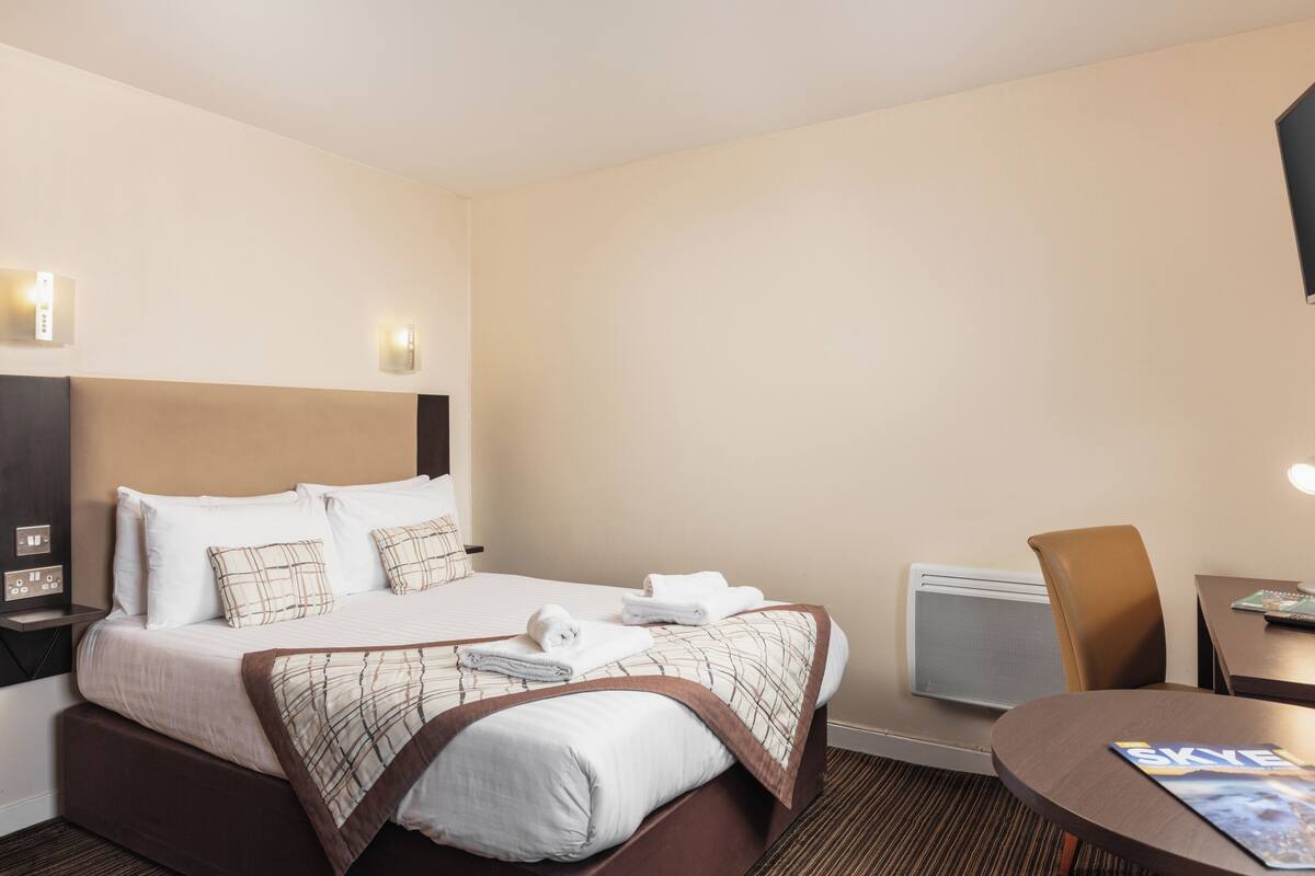 A hotel room with a neatly made bed, a desk with a chair, and a wall-mounted TV.